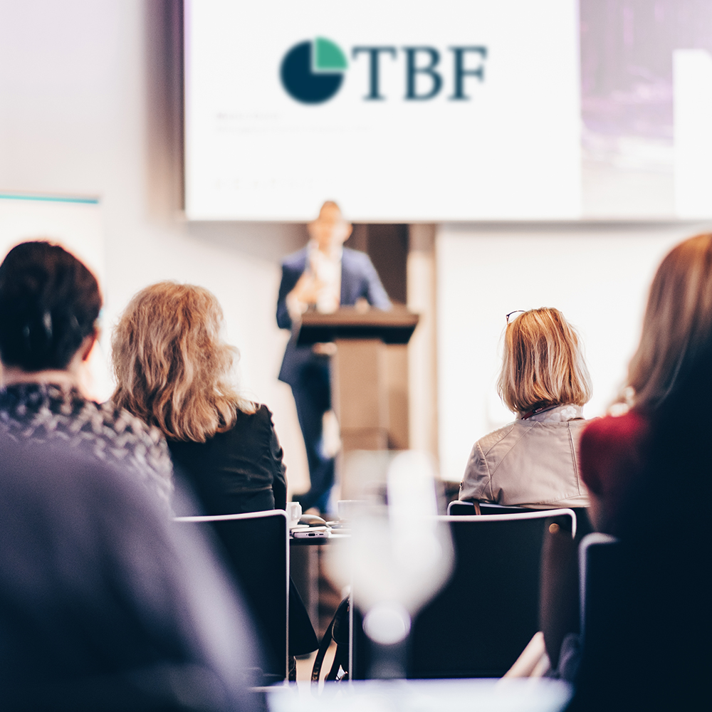 Das Bild zeigt sitzende Leute bei einem Vortrag vor einer großen Leinwand mit einem Referent